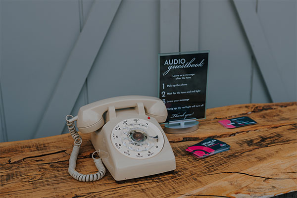 A hand reaching for a rotary phone handset on a pink background